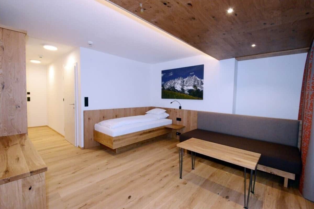 A modern room with a wooden floor, a bed with a wooden headboard, a bench, and a wall-mounted picture of a mountain.