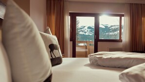 Habitación de hotel con una cama, vista a montañas nevadas a través de un ventanal grande y un balcón de madera.