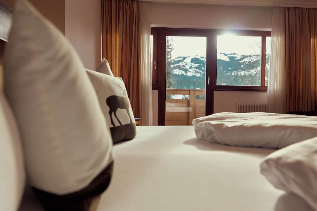 Une chambre d’hôtel avec un lit, une vue sur des montagnes enneigées par une grande fenêtre et un balcon en bois.