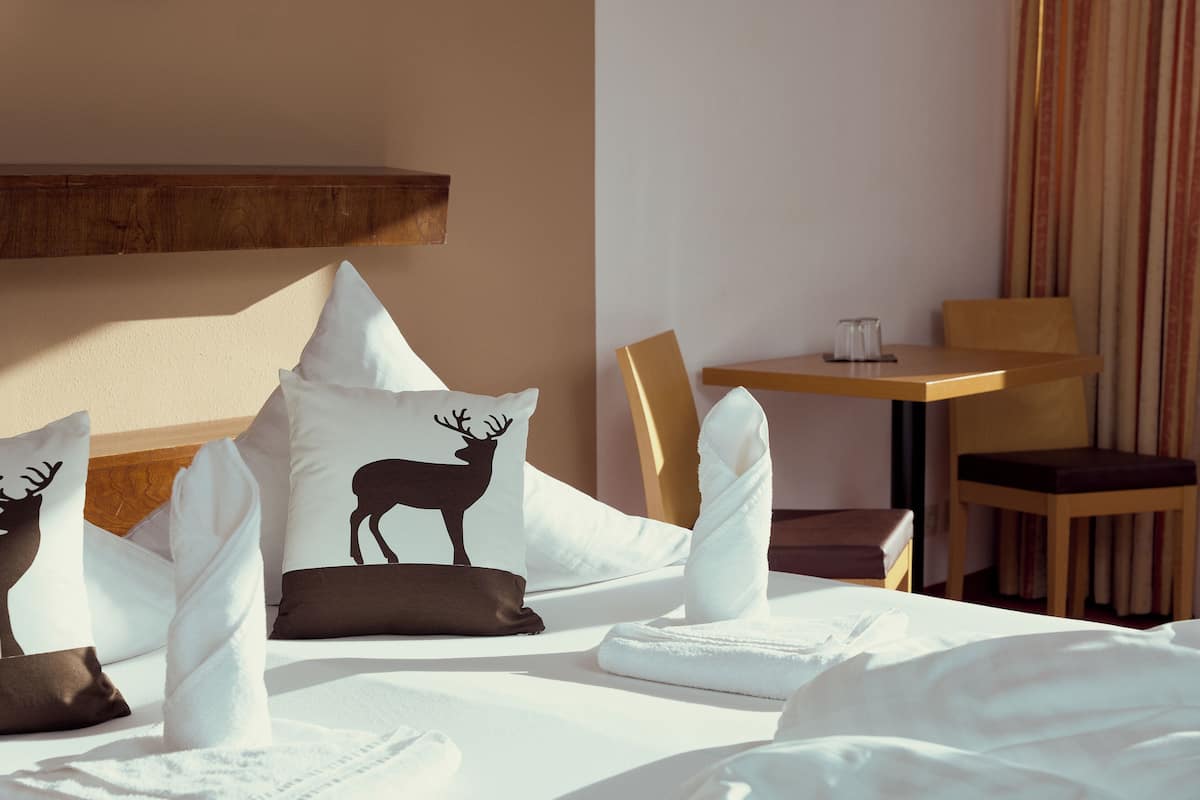 Une chambre d’hôtel avec un lit, des oreillers à motifs animaliers, une tête de lit en bois, une petite table et une chaise.
