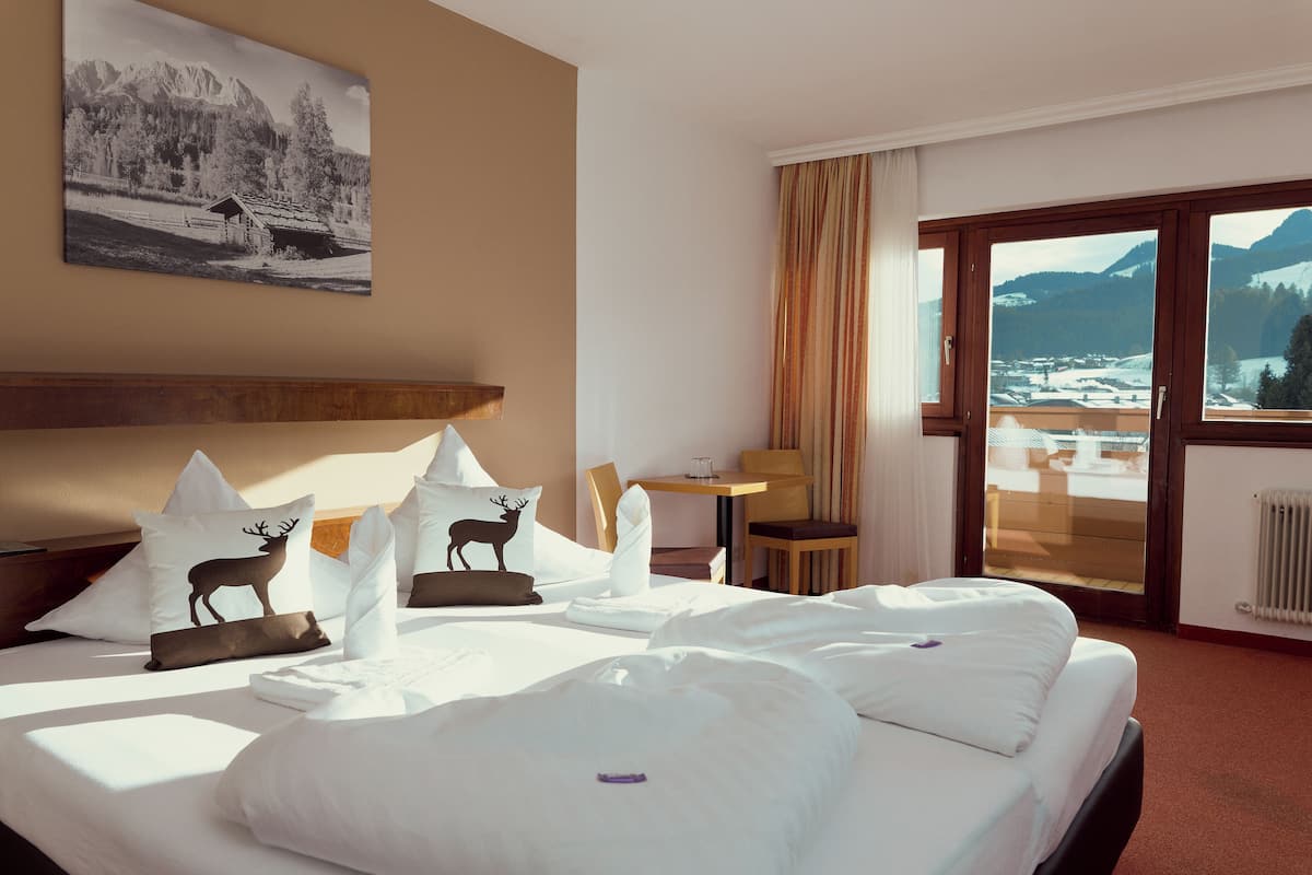 Une chambre d’hôtel équipée d’un lit, d’un bureau, d’une chaise et offrant une vue sur les montagnes par une grande fenêtre.
