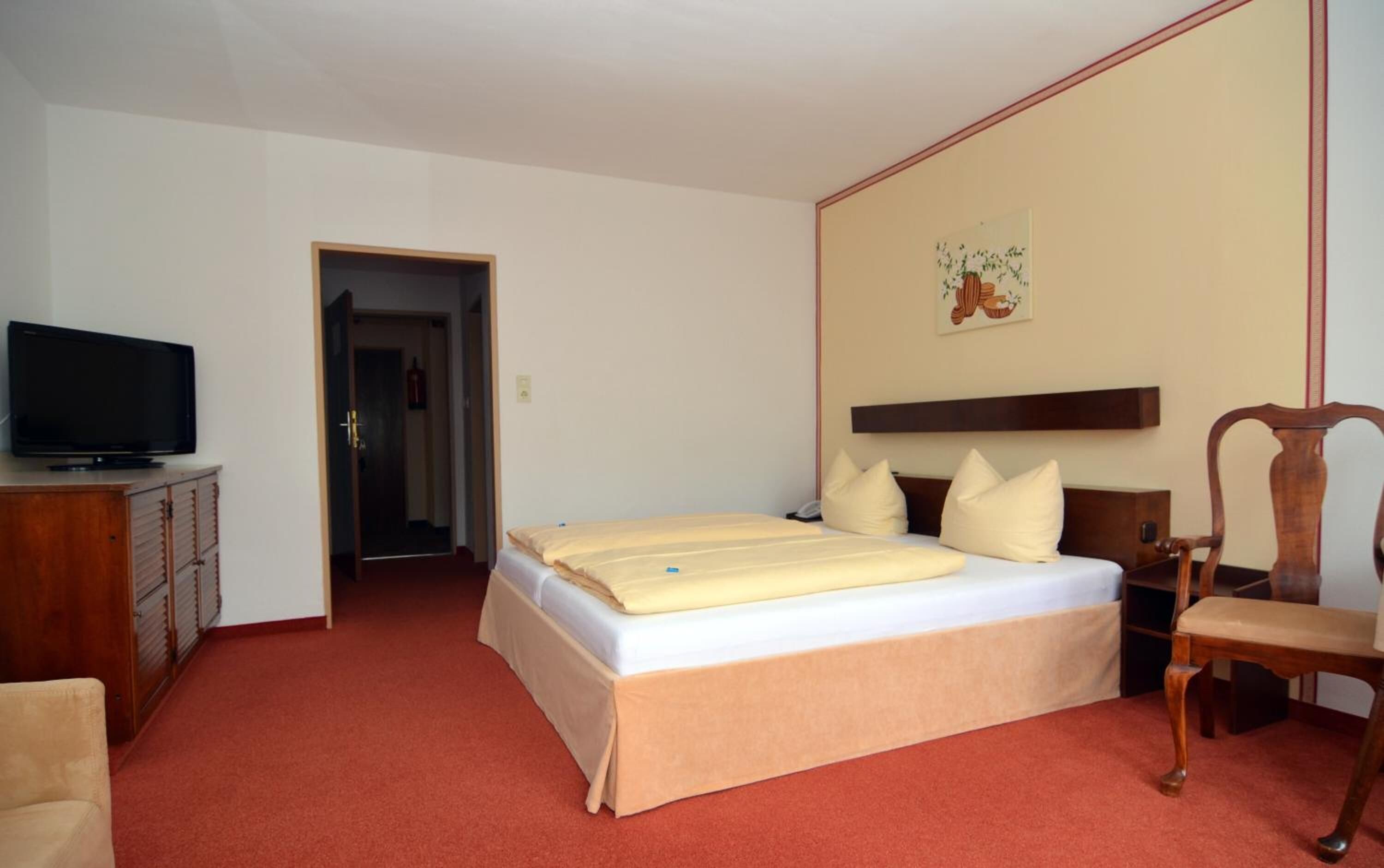 A hotel room with a bed, a television, a chair, and a door leading to another room.