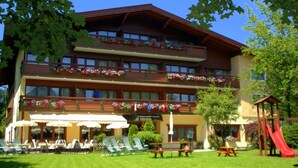 Un hotel de varios pisos con balcones decorados con jardineras, mobiliario exterior y una zona de juegos para niños.