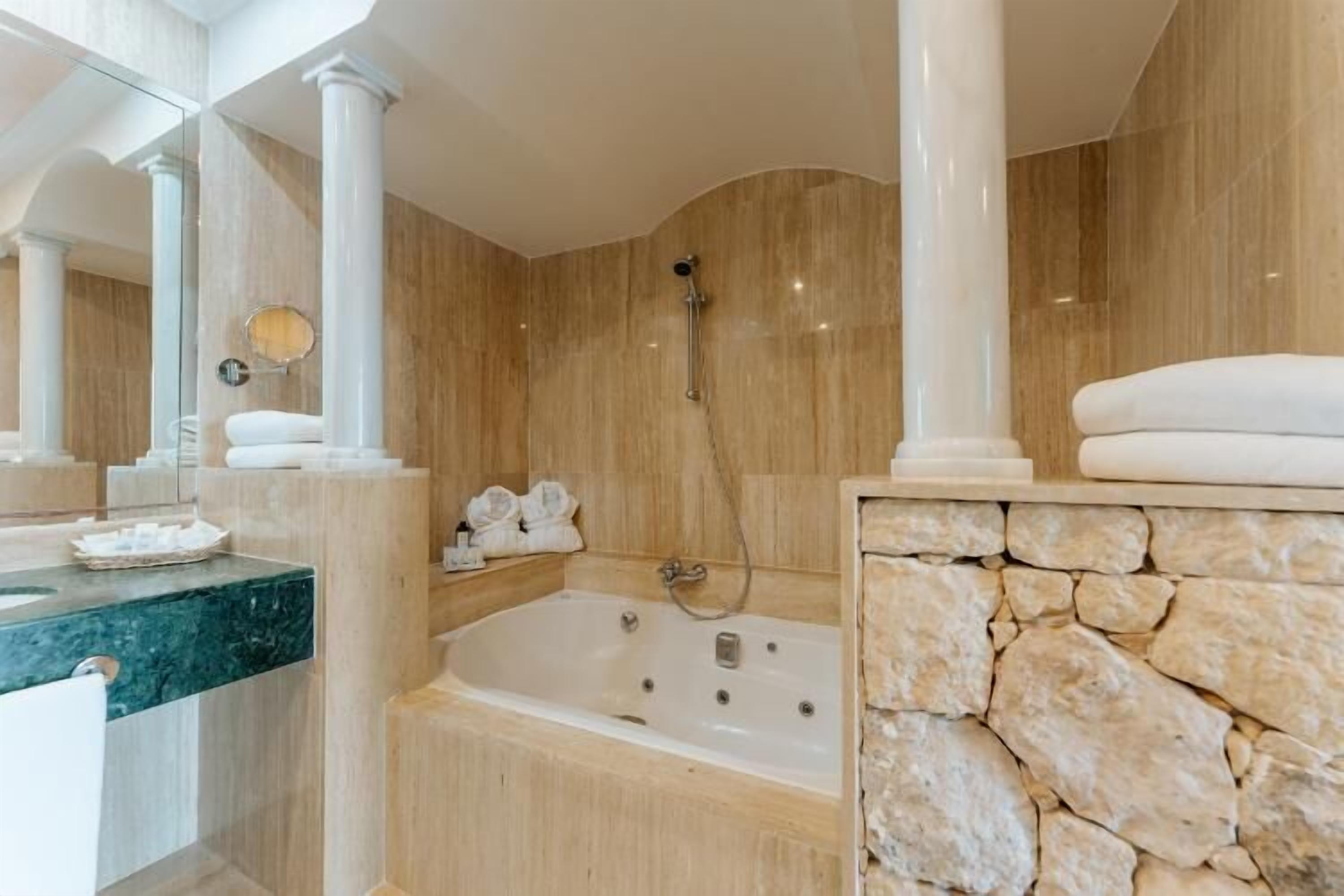 Un baño con bañera, espejo y pared de piedra.