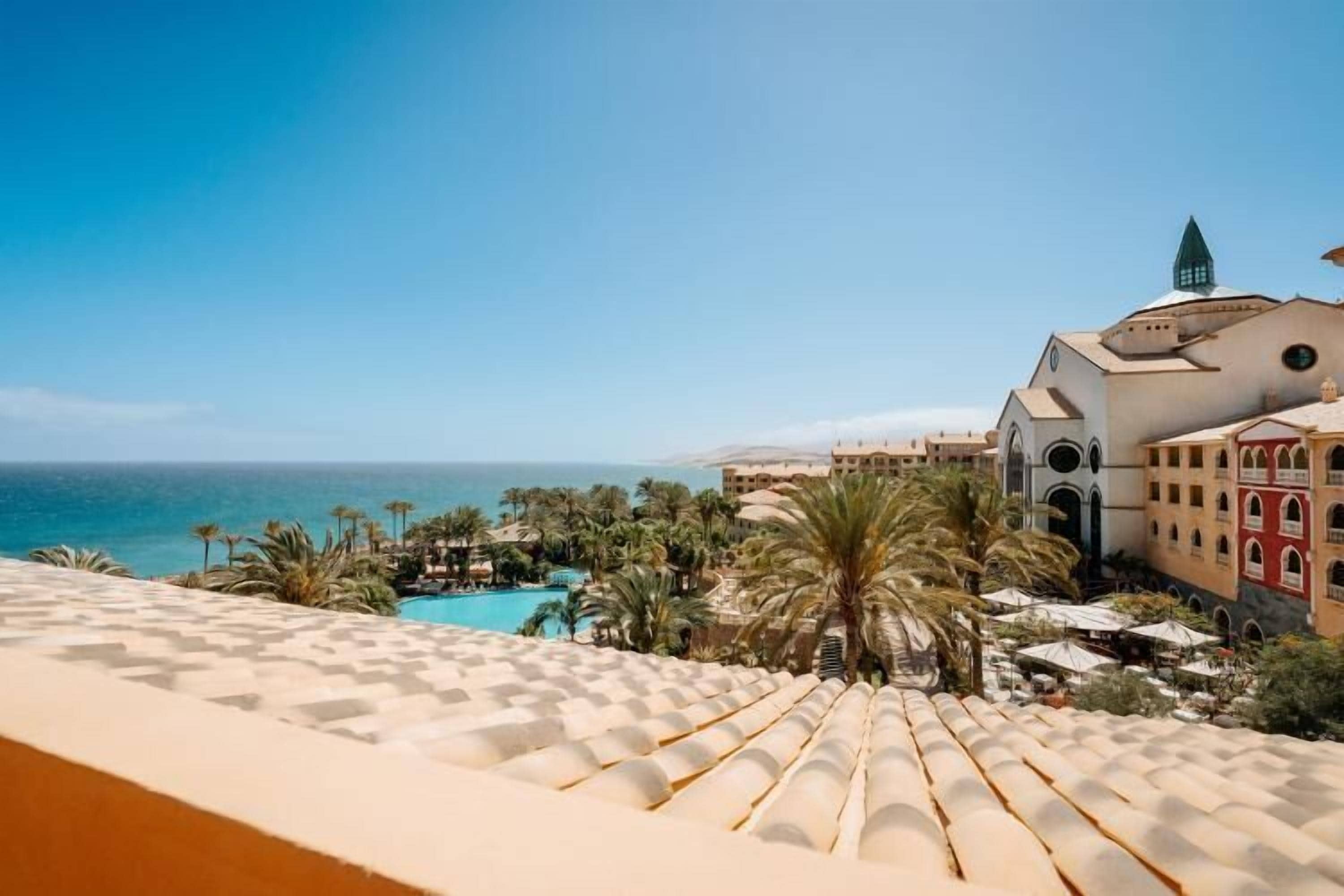 A resort with a pool, palm trees, and a view of the sea.