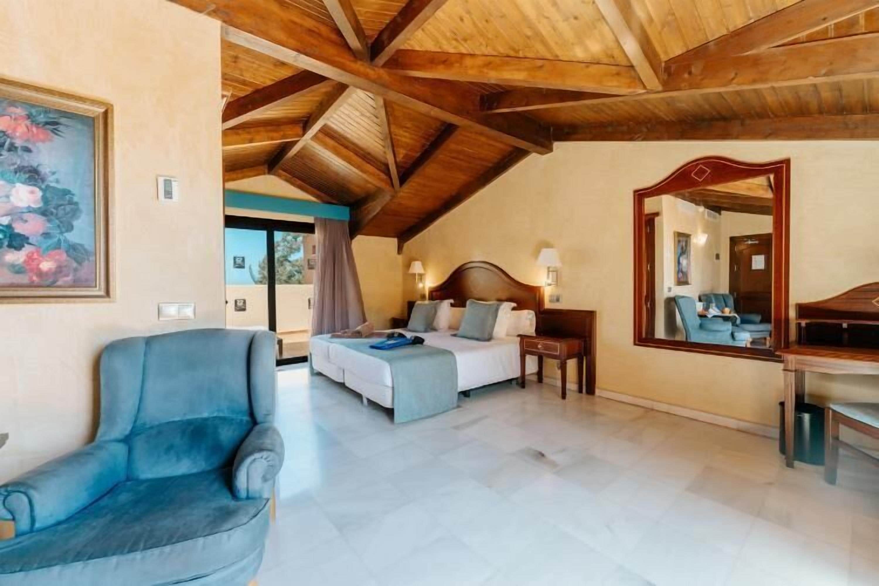Een slaapkamer met een bed, een stoel, een bureau en een grote spiegel.