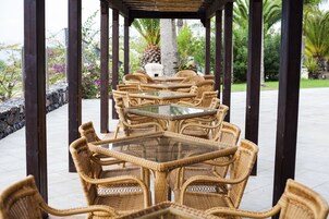 A covered outdoor seating area with wicker furniture and glass-top tables.