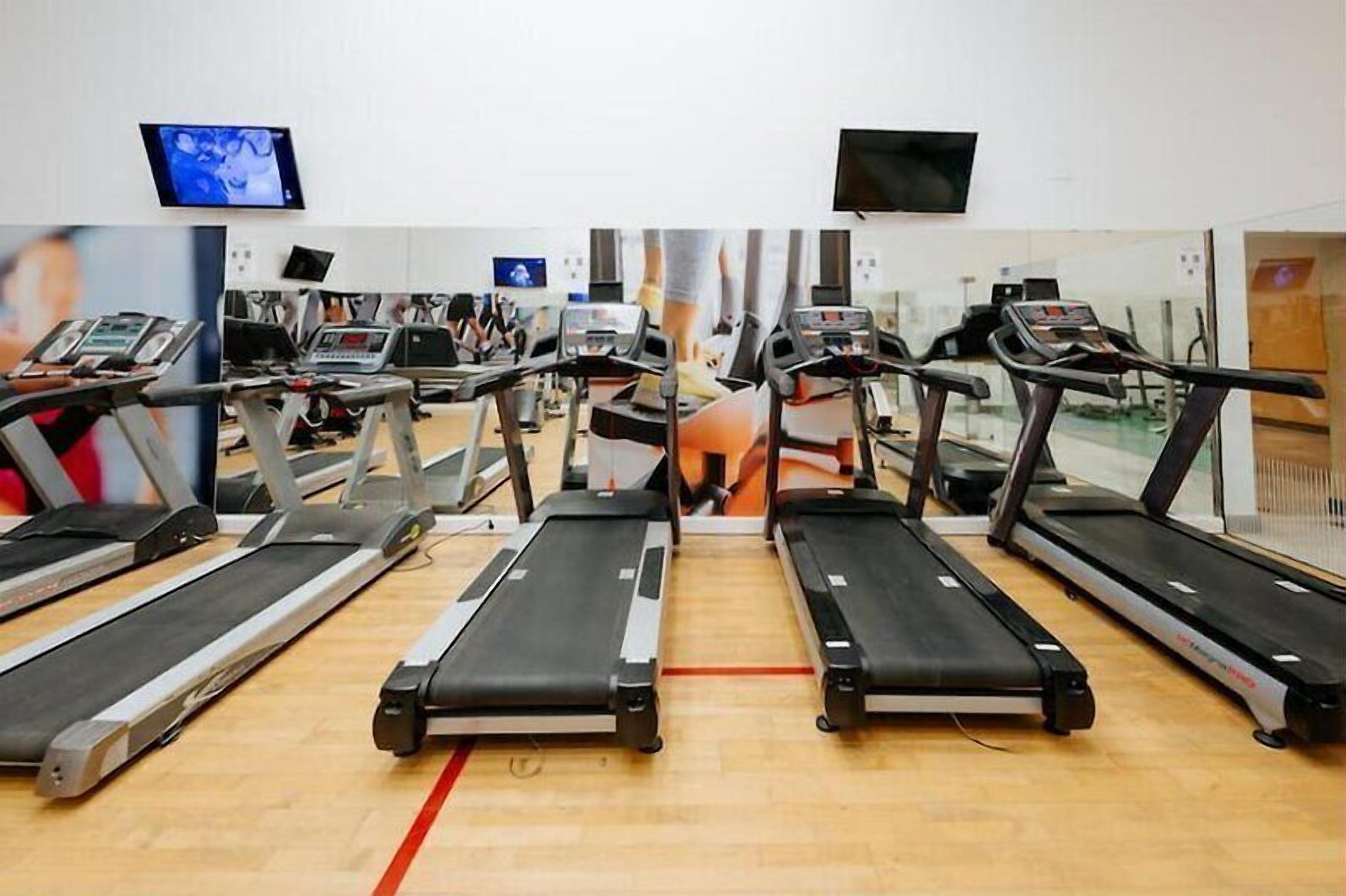 Una palestra con diverse tapis roulant, uno schermo televisivo e uno specchio.