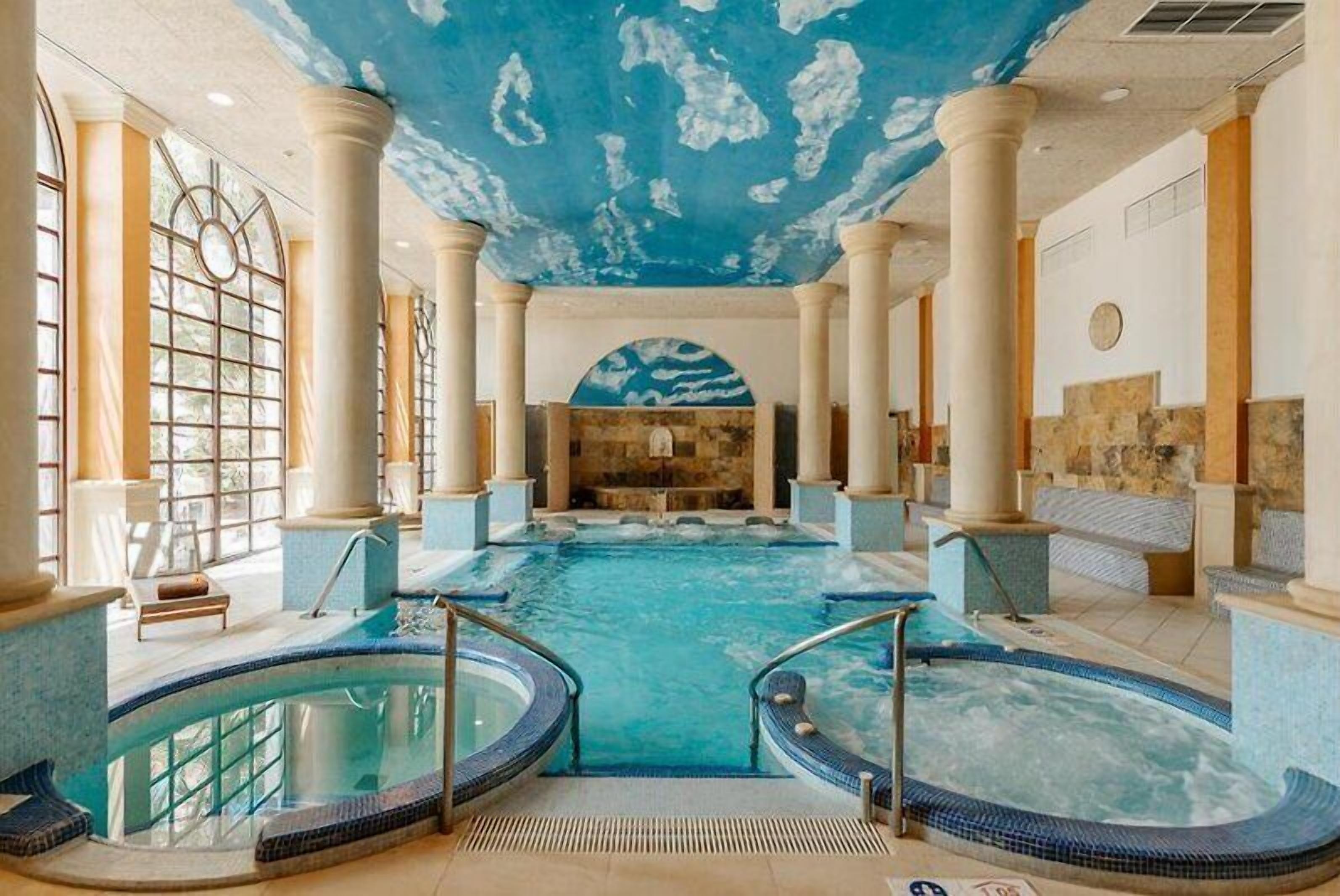 A large indoor swimming pool with multiple lanes, surrounded by columns and a stone wall.