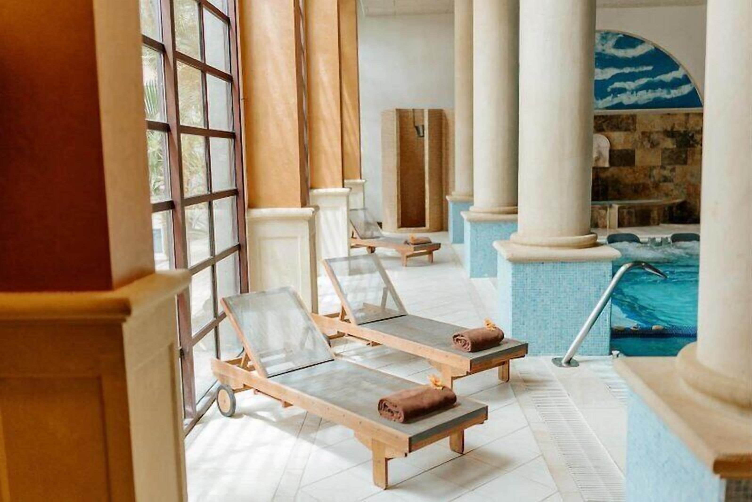 Ein sonnendurchfluteter Poolbereich mit Liegestühlen, einem kleinen Pool und Blick ins Freie.