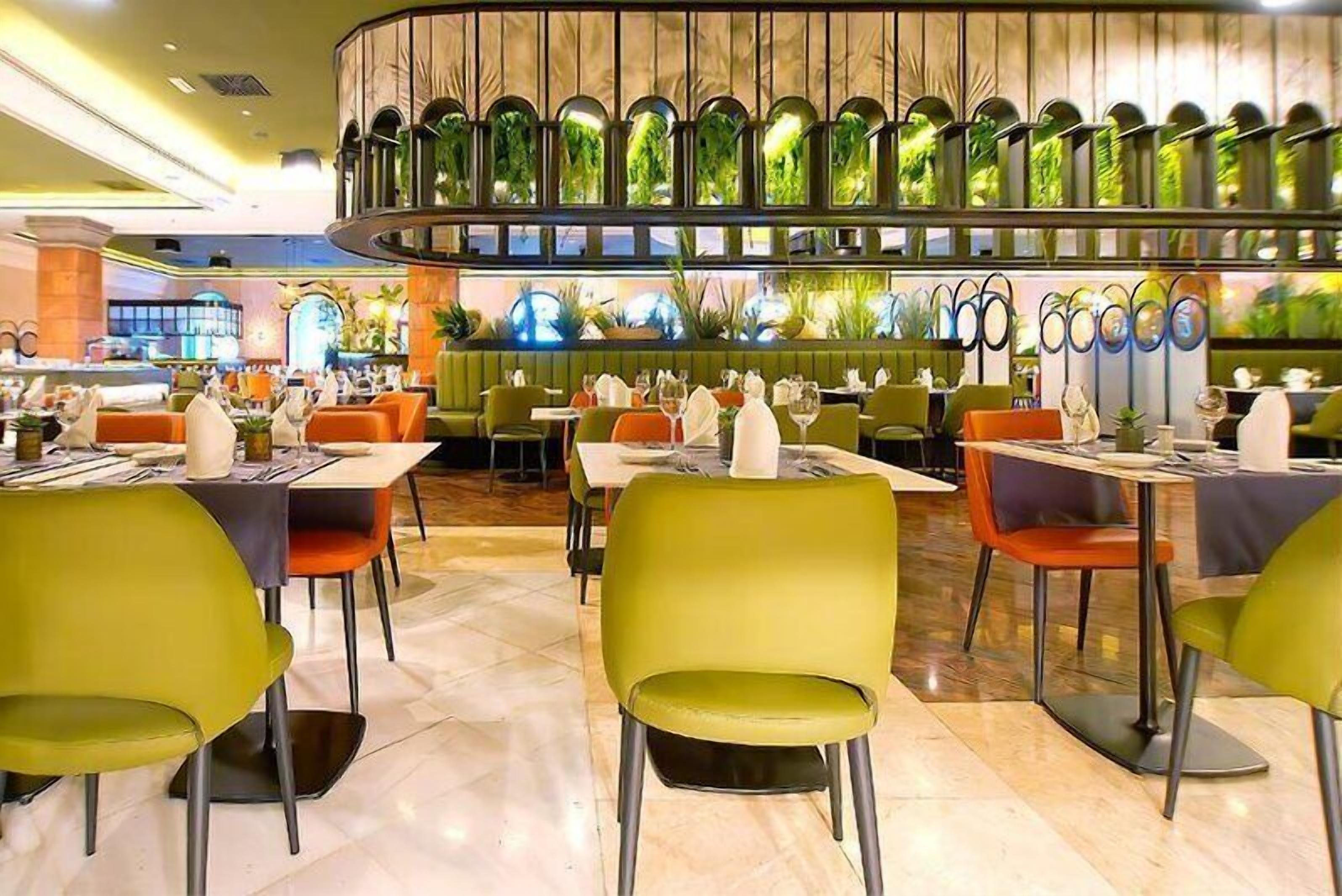 En restaurang med flera bord och stolar, en centralt placerad dekorativ detalj med växter och en modern inredning.