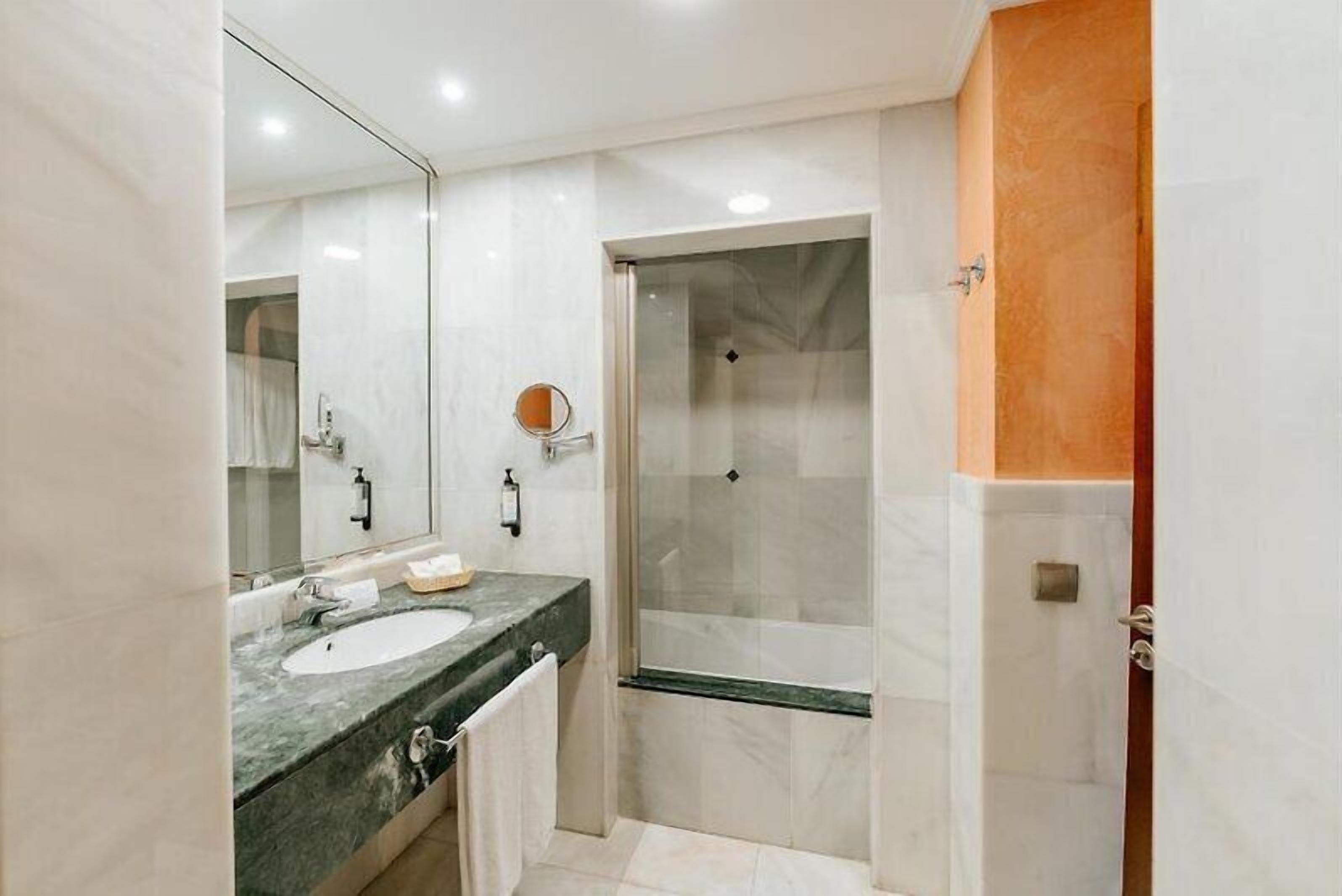 Un baño moderno con ducha de vidrio, un espejo grande y encimera de mármol.
