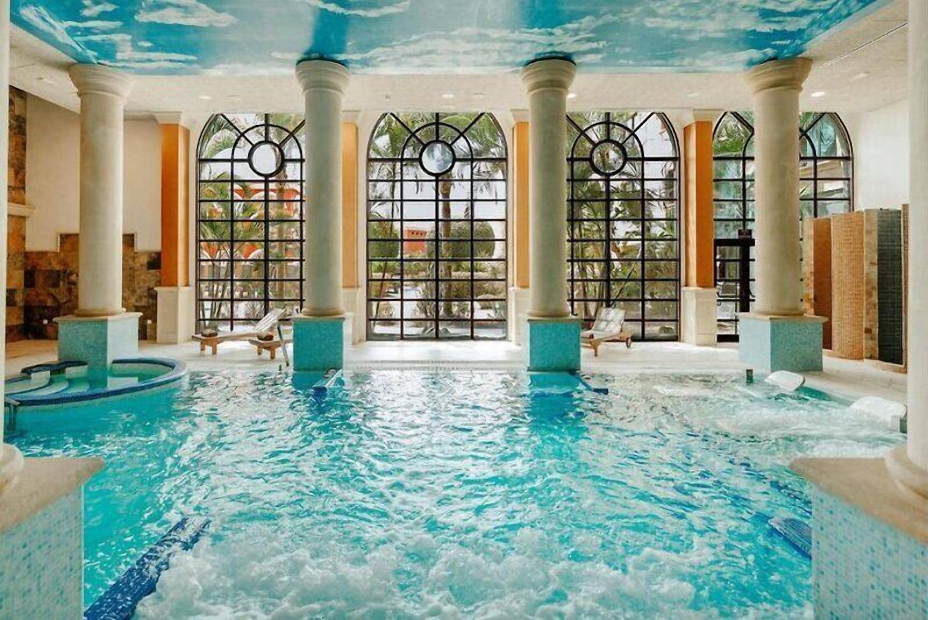 An indoor swimming pool with clear water, surrounded by columns and large windows.