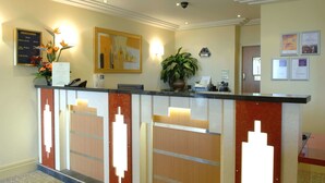 Ein moderner Hotelrezeptionstresen, mit einer Pflanze und gerahmten Kunstwerken an der Wand.