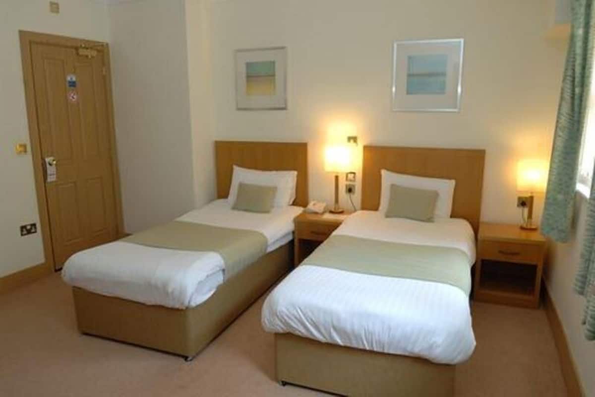 Et hotelværelse med to enkeltsenge, en trædør, sengeborde med lamper og billeder i rammer på væggene.