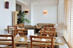 Un comedor de hotel con mesas y sillas de madera, un atril para el menú y una planta.