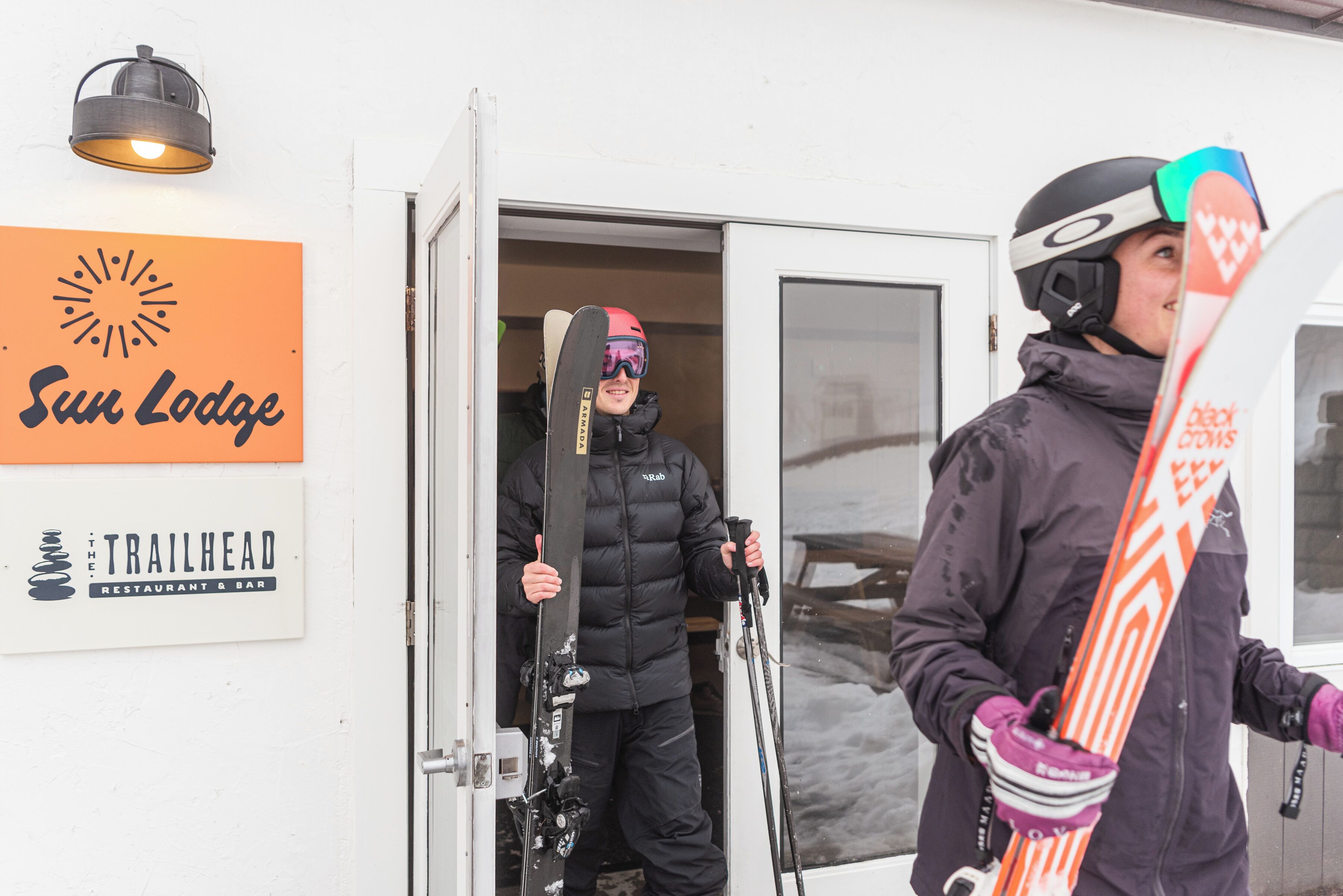 A person exiting a vehicle with skis, a snowboard, and a helmet.