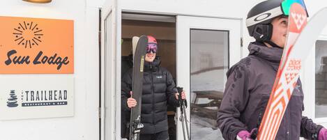 A person exiting a vehicle with skis, a snowboard, and a helmet.