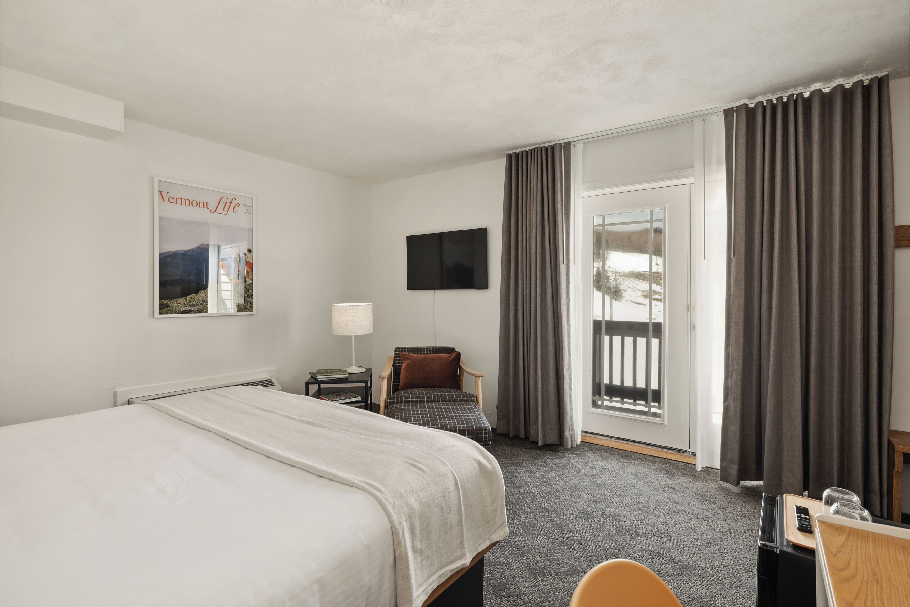 A hotel room with a bed, a chair, a desk, a TV, and a window with curtains.