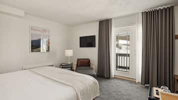 Habitación de hotel con cama, una silla, escritorio, televisión y ventana con cortinas.