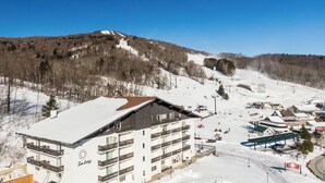 A multi-story hotel with balconies, a ski slope in the background, and a clear blue sky. - Sun Lodge near Manchester VT, Ascend Collection Hotel (Peru)
