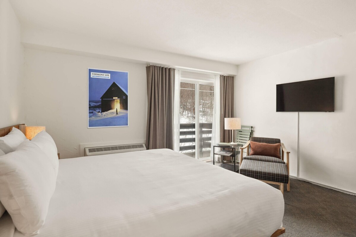 Habitación de hotel con una cama grande, televisión de pantalla plana, una silla y un cartel en la pared.