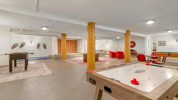 A room with a foosball table, a pool table, and red chairs.