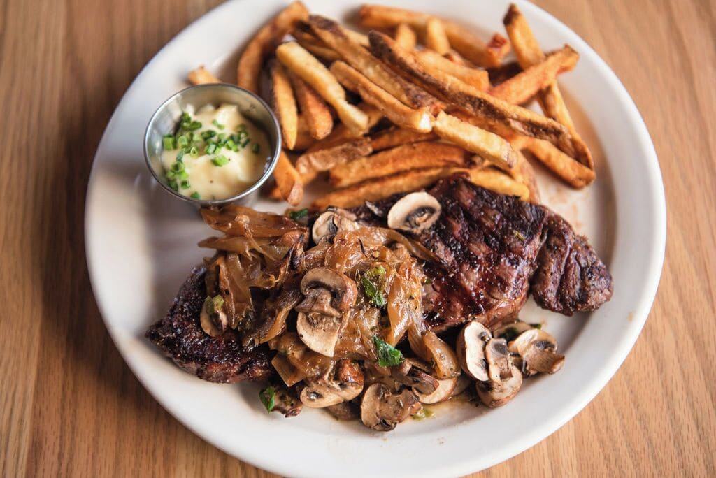 Ein Teller mit Steak, Pilzen, Pommes und einer kleinen Saucenschale.
