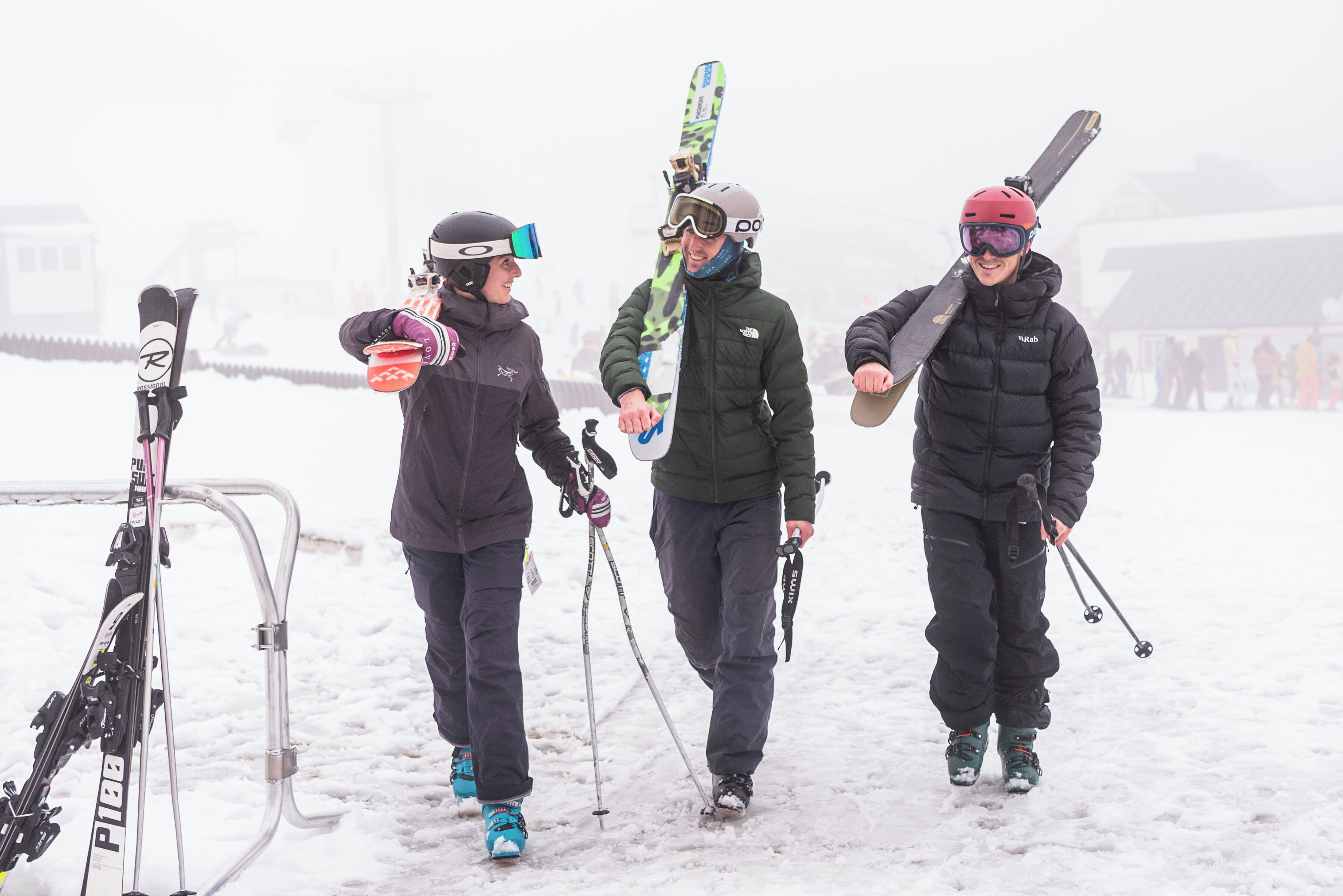 Tres personas caminando sobre la nieve, cada una llevando esquíes y bastones.