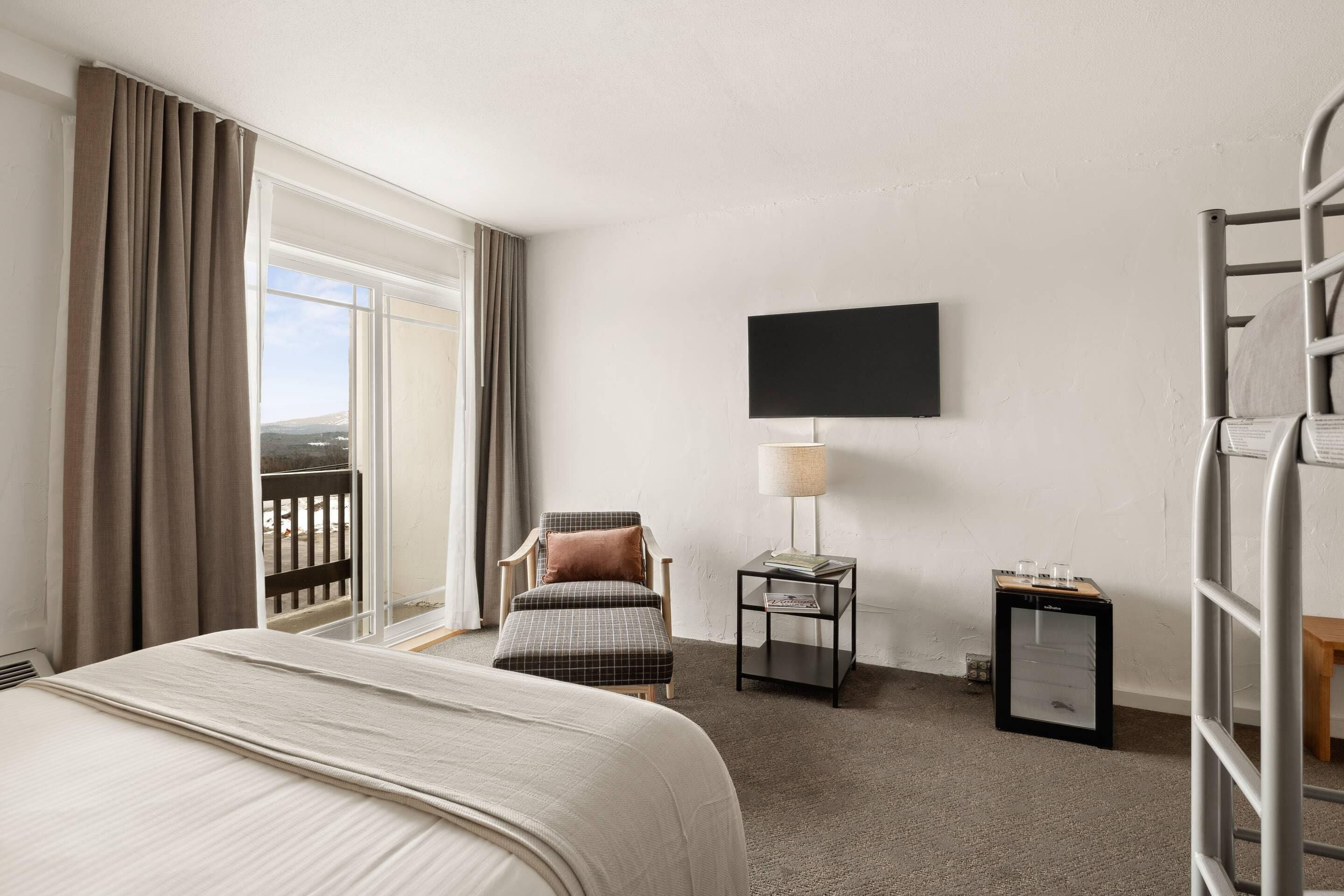 A hotel room with a bed, a chair, a TV, a lamp, and a small table.