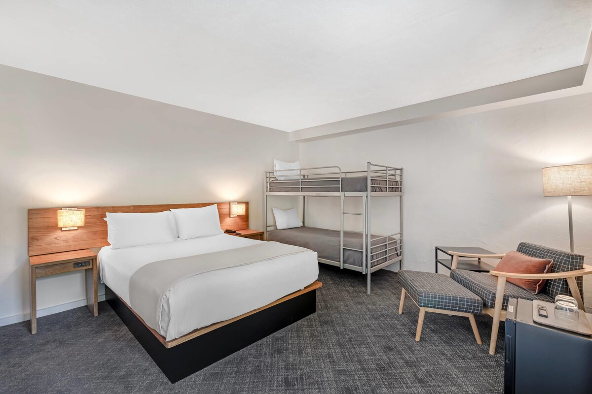 Habitació d'hotel amb un llit individual, una lliterà i un estenent, una cadira i una taula petita.
