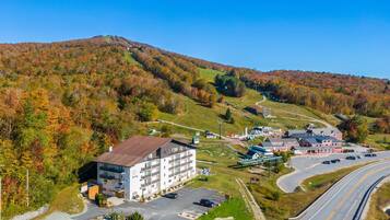 A hotel with a parking lot, a ski lift, and a mountainous backdrop.