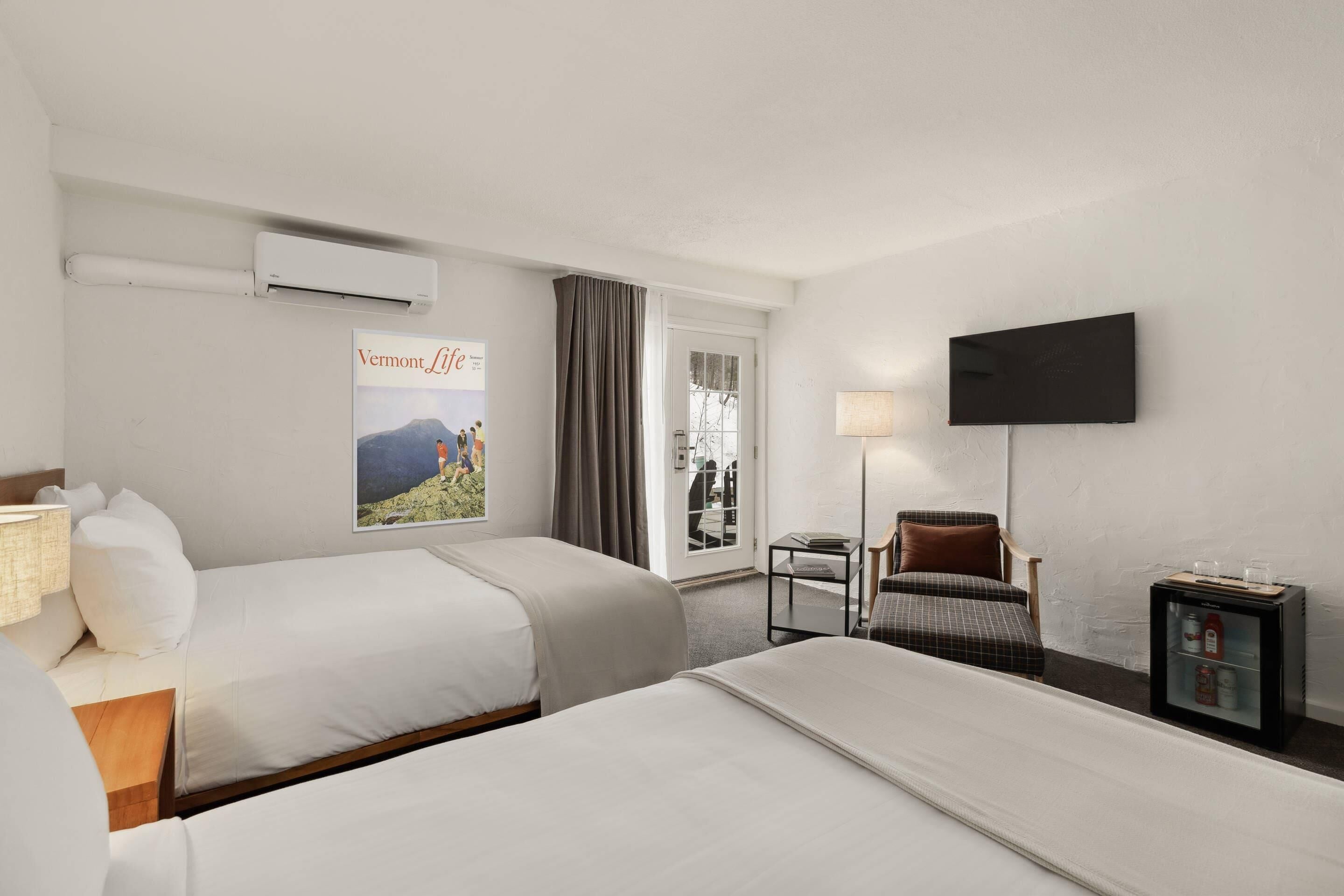Ein Hotelzimmer mit zwei Betten, einem Flachbildfernseher, einem kleinen Tisch, einem Stuhl und einer Minibar.