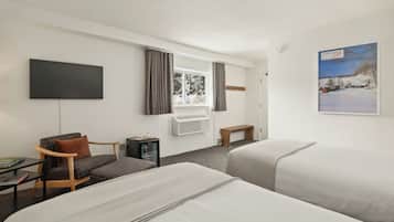 Une chambre d’hôtel avec deux lits, un bureau, une chaise, une télévision et une fenêtre avec des rideaux.