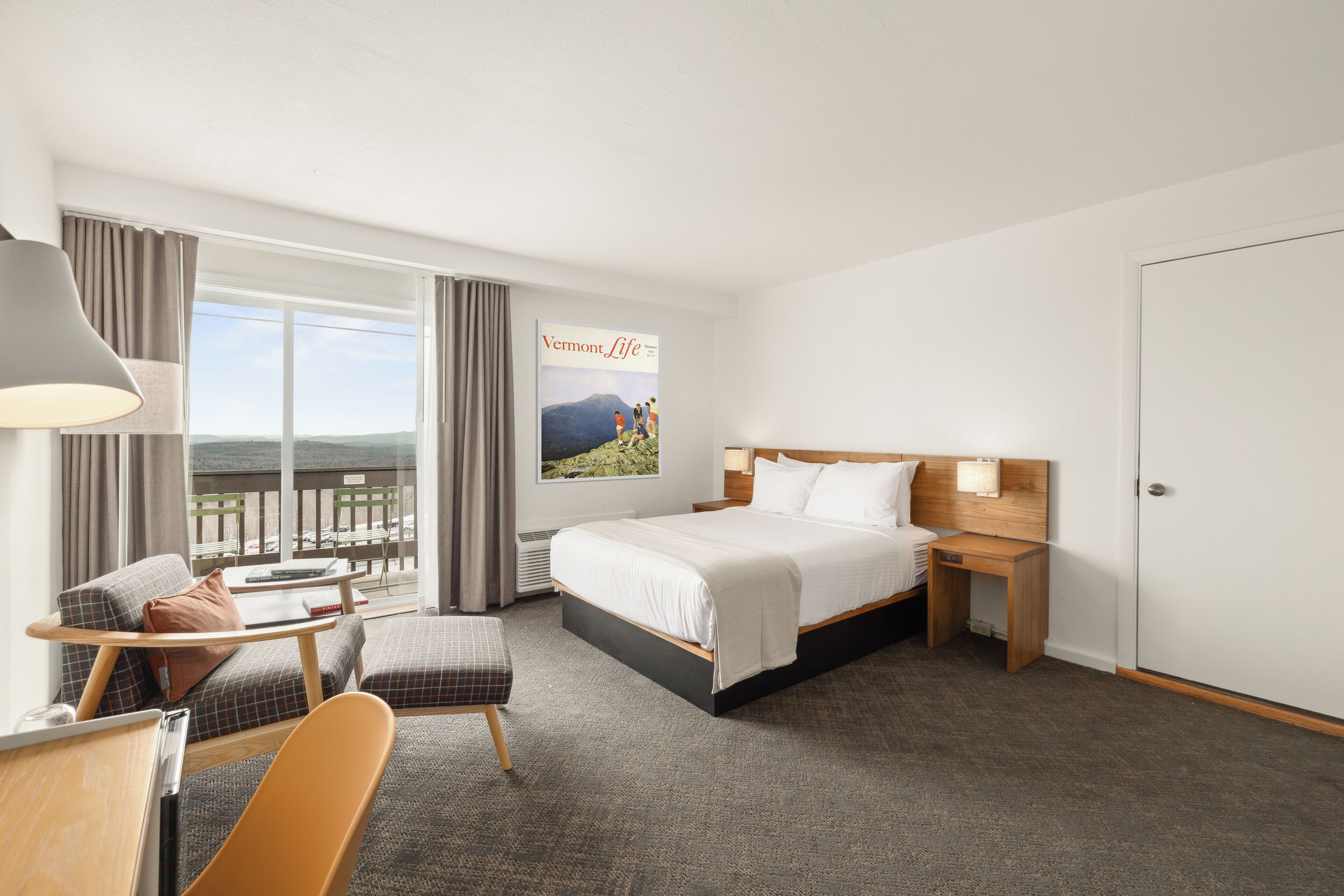 Hotelkamer met een bed, een bureau, een stoel, een nachtkastje en een groot raam met uitzicht op de omgeving.