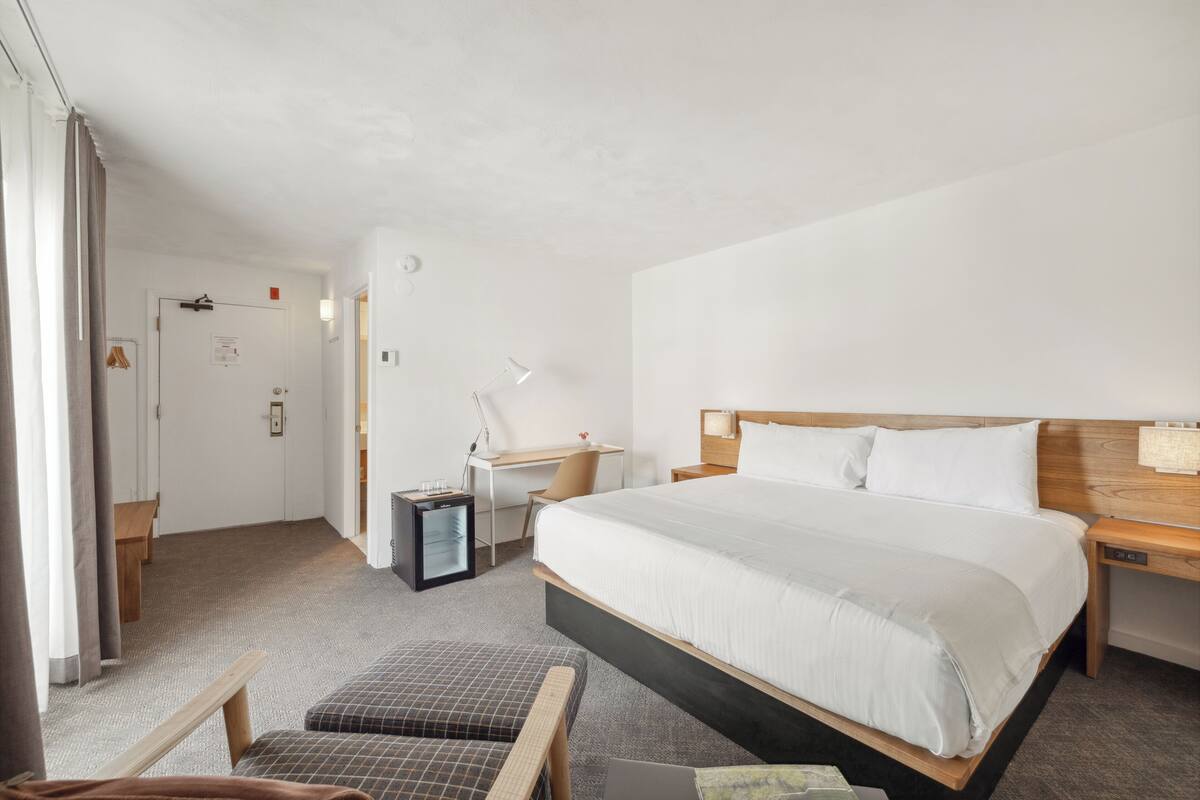 A hotel room with a large bed, a desk, a chair, and a small table.