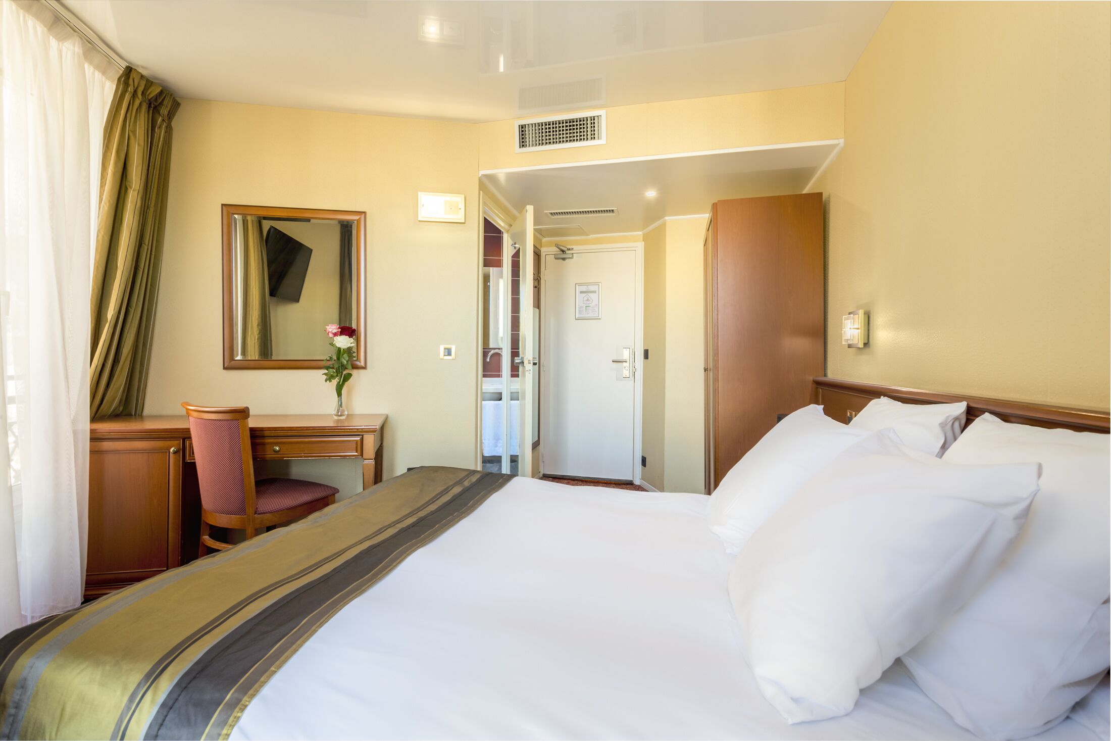 Habitación de hotel con una cama grande, un escritorio con una silla, un espejo y una puerta que da a un baño.