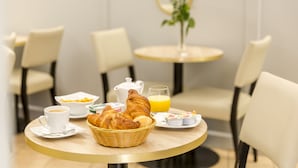 A breakfast setting with croissants, coffee, orange juice, and a vase of flowers on a round table. - Hotel Berkeley (Paris)