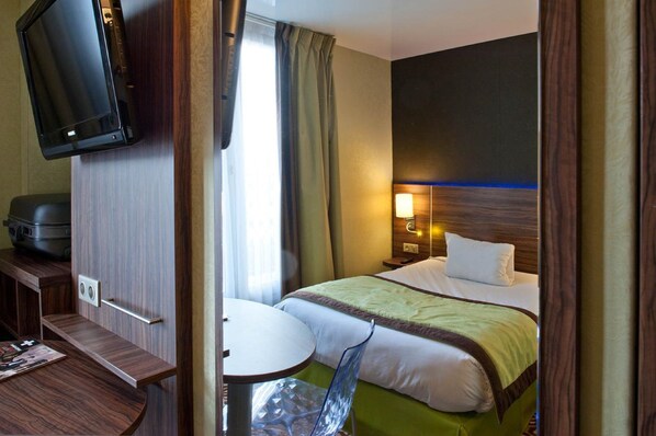 A hotel room with a bed, bedside table, lamp, TV, and a small seating area with a chair and table.