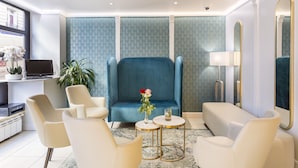 A modern hotel room with a large blue sofa, white armchairs, a small round table, and a potted plant. - Hotel Berkeley (Paris)