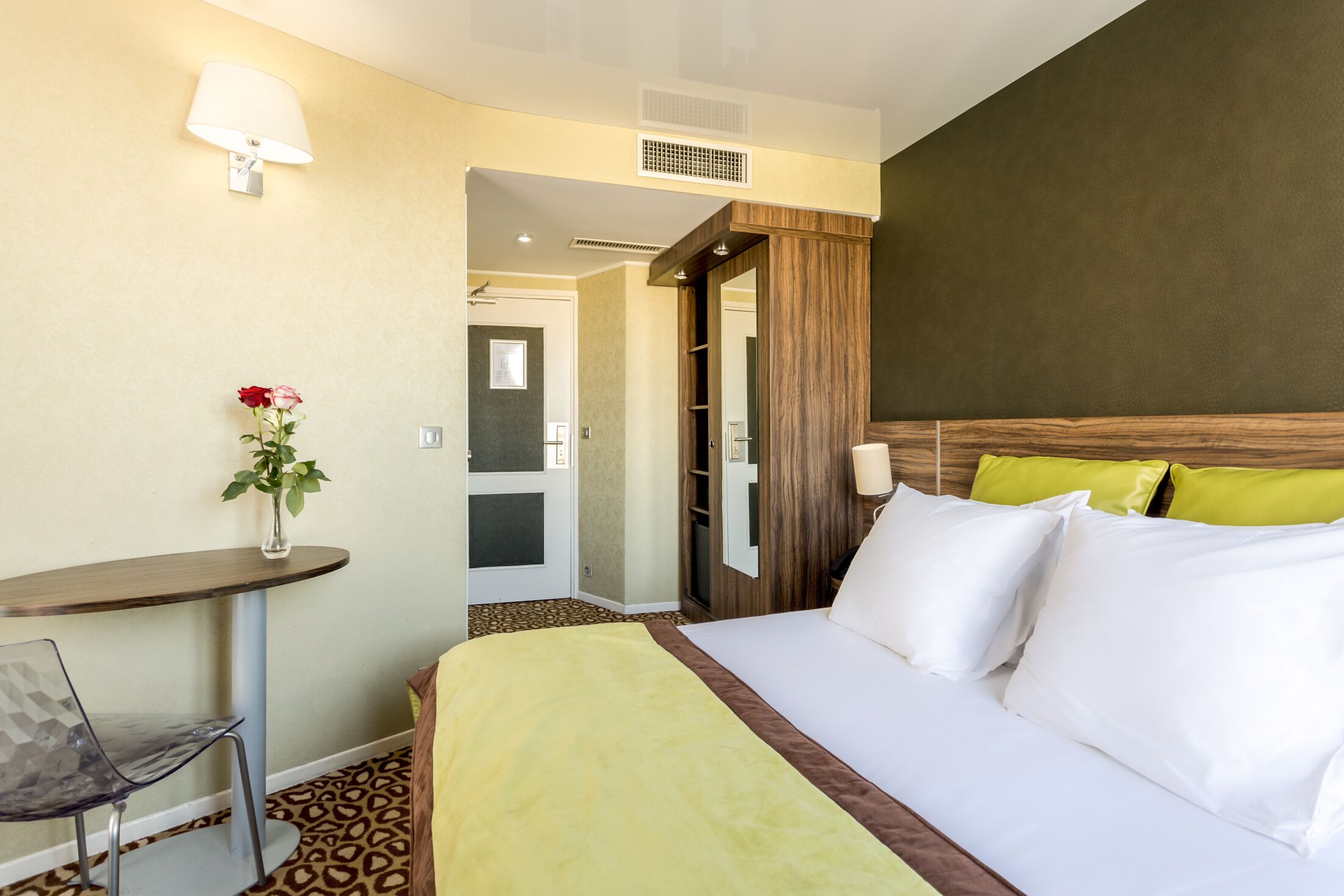 Una habitación de hotel con cama, escritorio, silla y un florero con flores.
