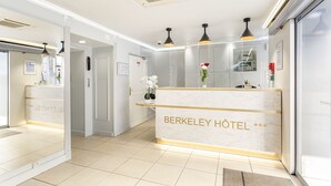 A hotel reception area with a marble counter, pendant lighting, and a digital clock. - Hotel Berkeley (Paris)