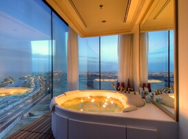 Un baño lujoso con una bañera grande, un espejo y vistas a un paisaje urbano.