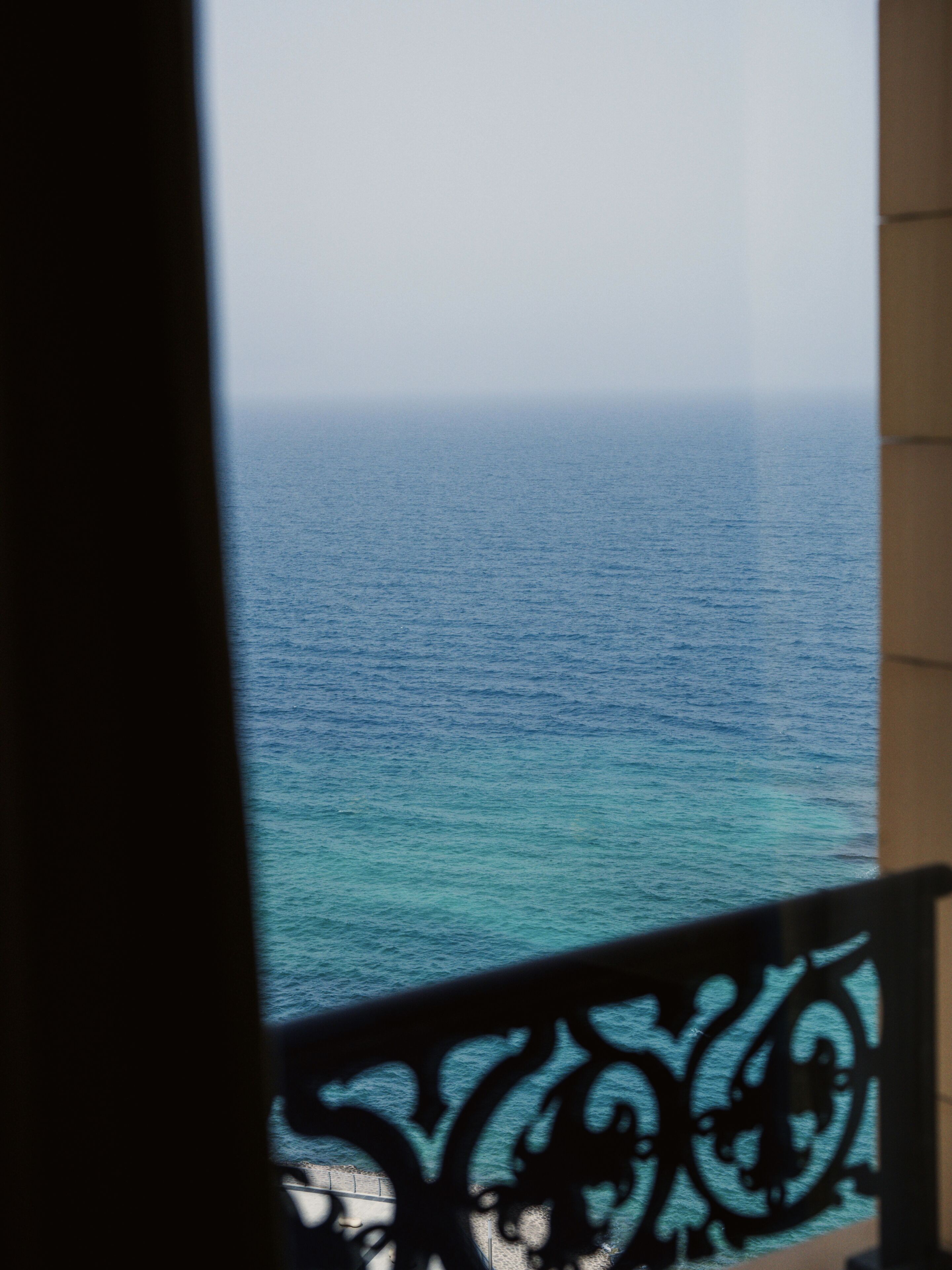 A view of the sea through a window with a decorative metal railing.