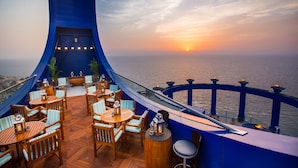 Een terras met houten meubels en uitzicht op de ondergaande zon boven de oceaan.