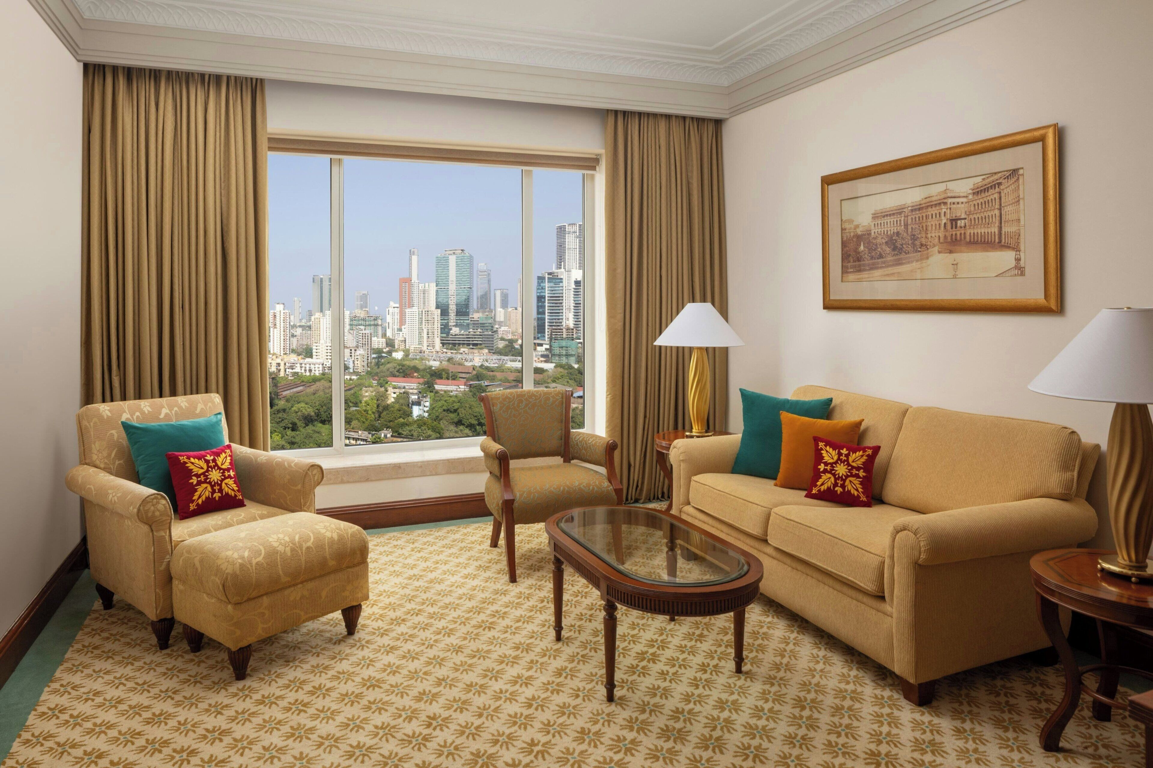 Una habitación de hotel con un ventanal grande, un sofá, dos sillones, una mesa de centro y una lámpara.