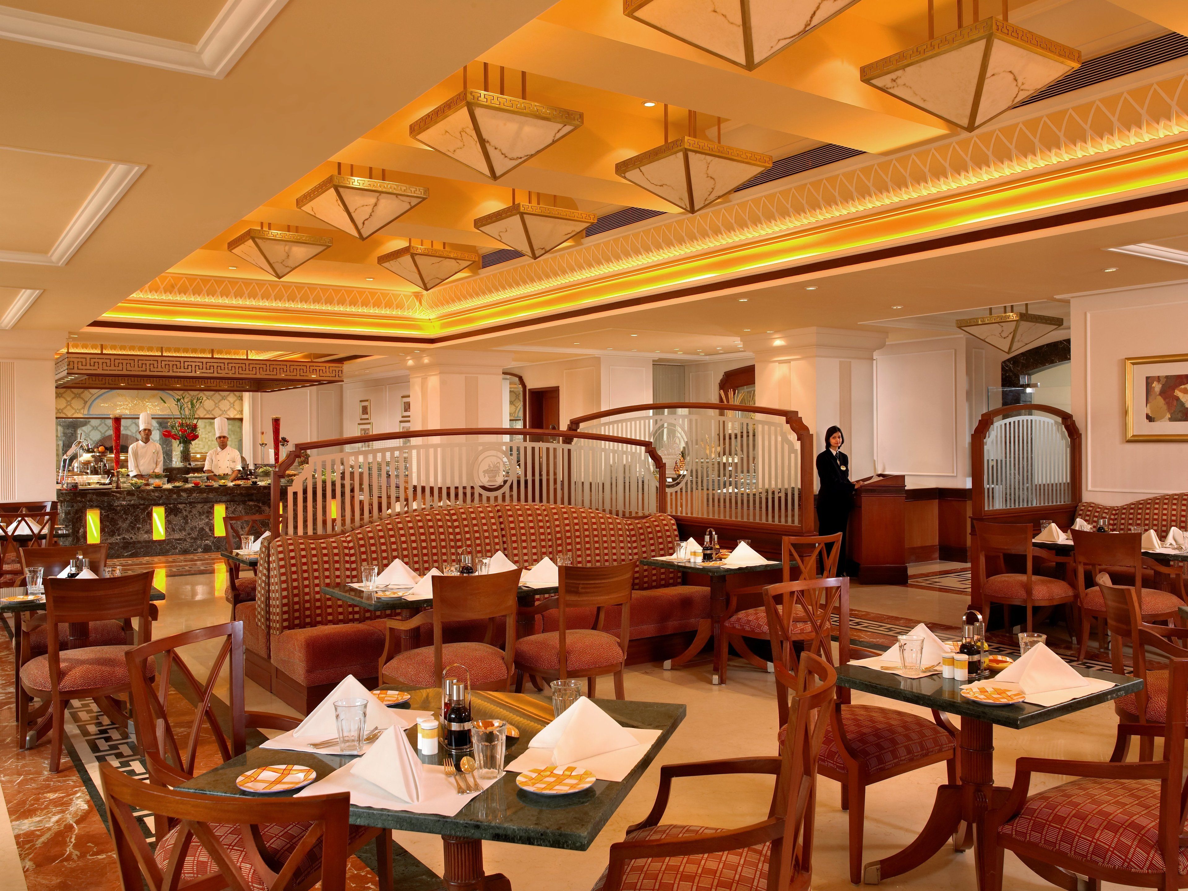 Un restaurante espacioso con techos altos, candelabros ornamentados y una zona central de asientos con bancos acolchados rojos.