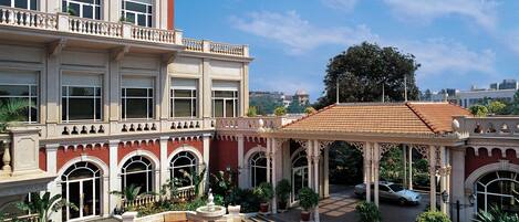 Un patio con una fuente, suelo de tejas rojas y un edificio con ventanas y balcones de arco.
