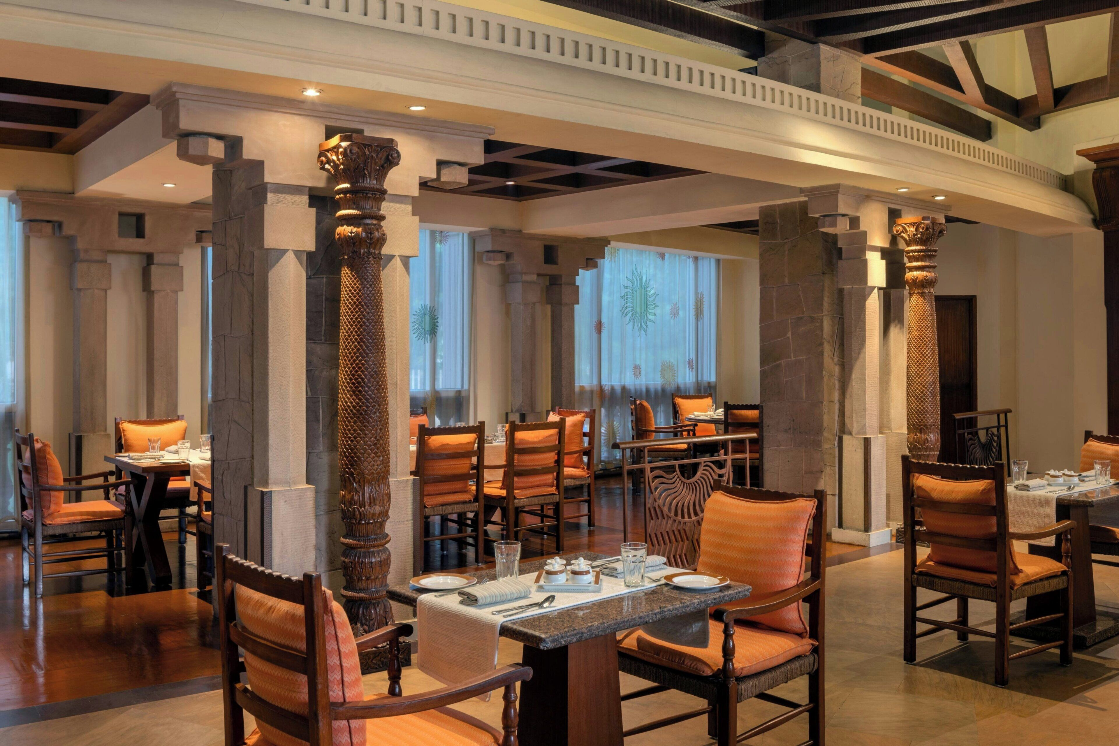 A spacious dining area with multiple tables and chairs, featuring ornate columns and a high ceiling with exposed beams.