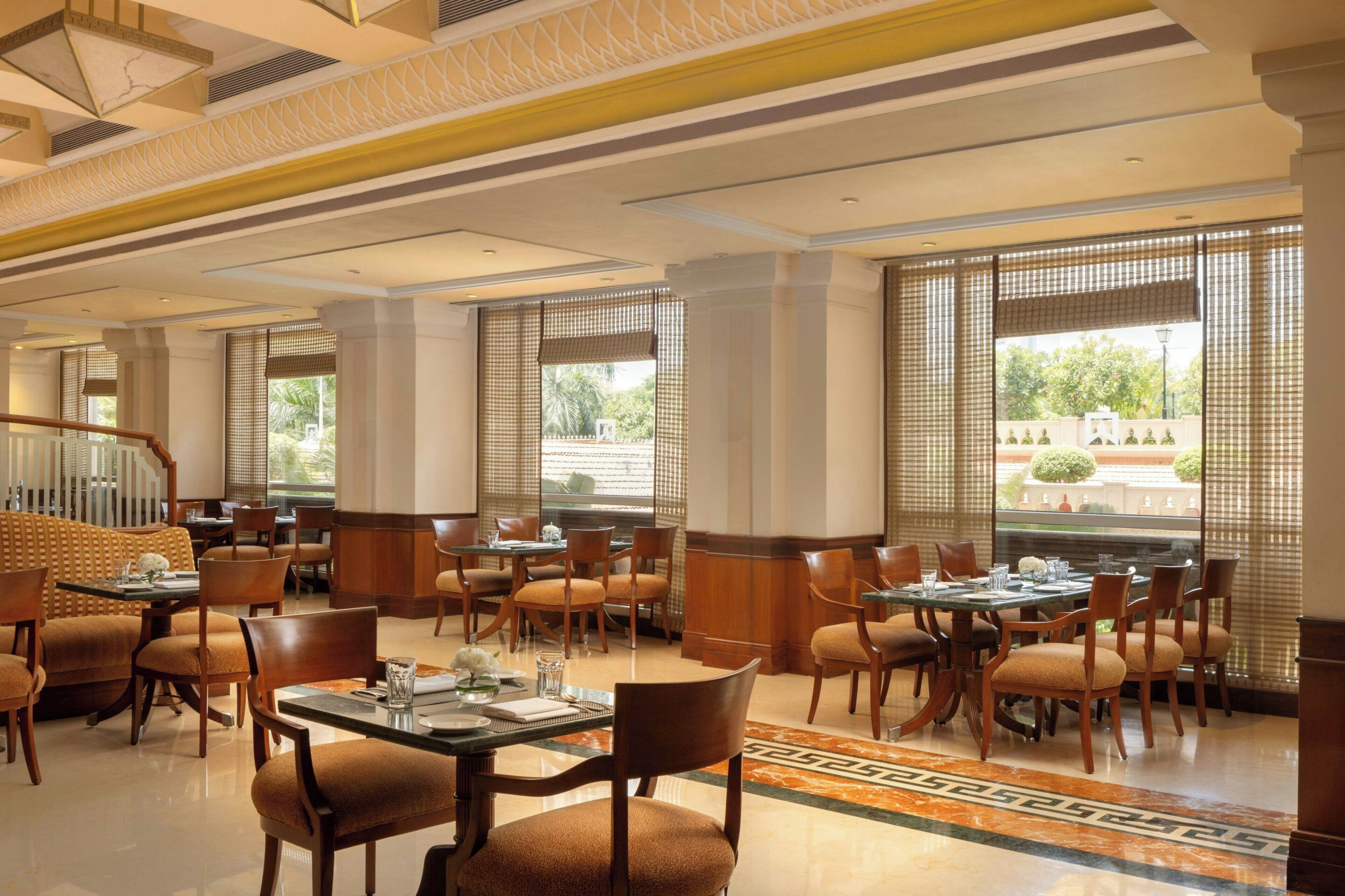 Un vaste espace dédié à la salle à manger, avec de nombreuses tables et chaises, de grandes fenêtres équipées de stores et un plafond décoratif.